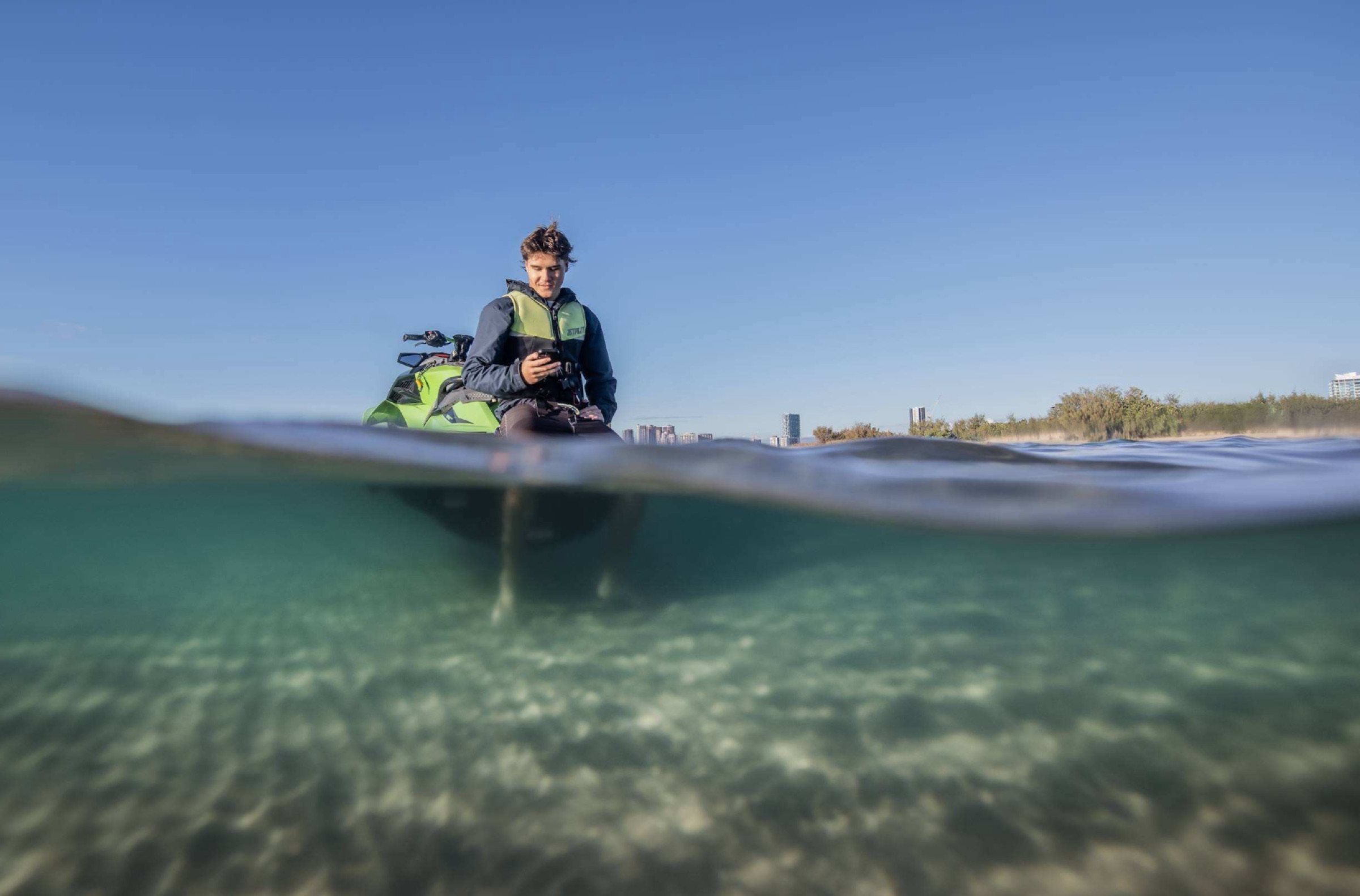 Fraser on a jet ski in clear shallow water, checking GoCoast on a phone